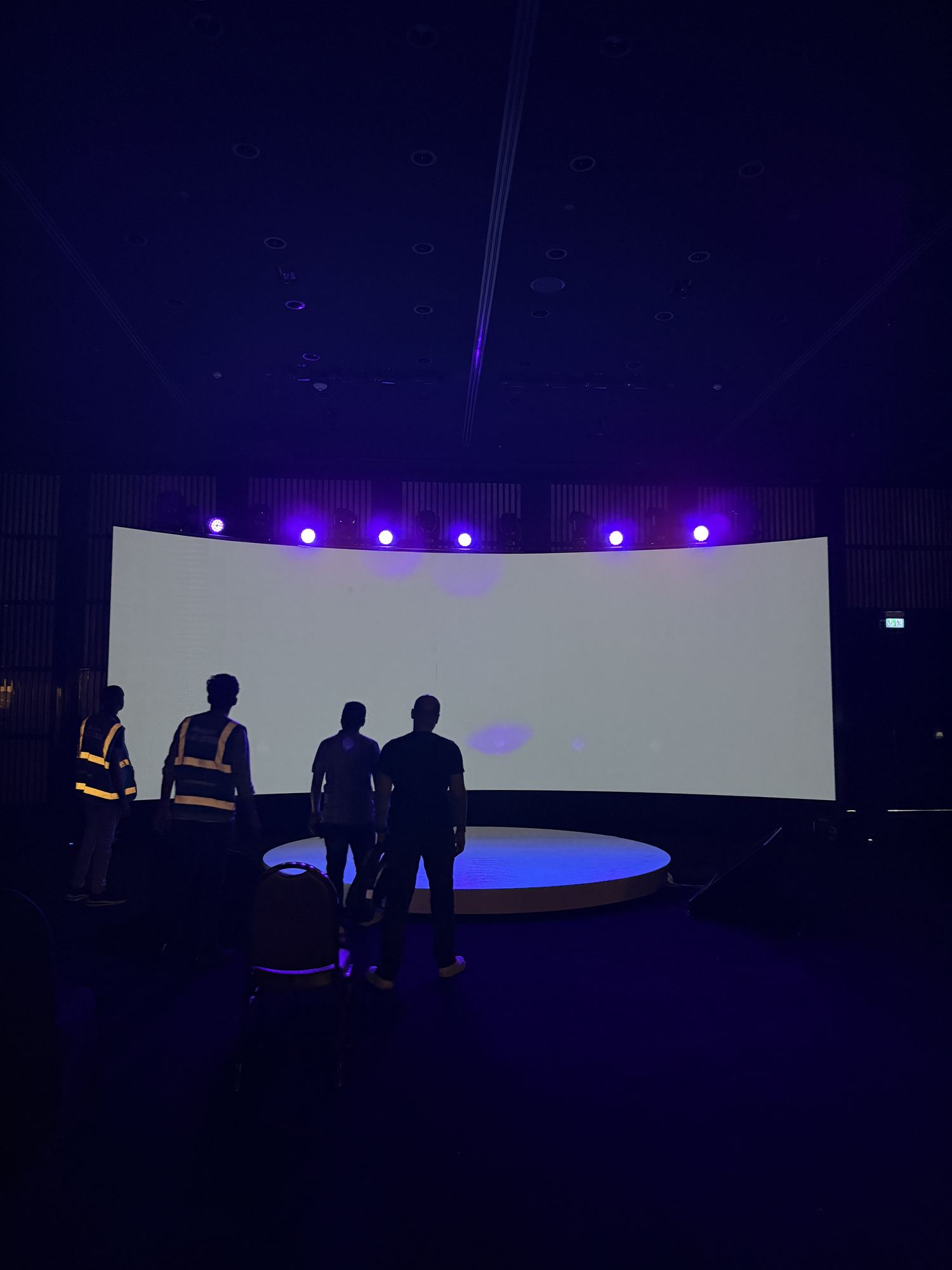A delivered gathering environment before the doors open: low seating, a dark stage wall and one lit screen